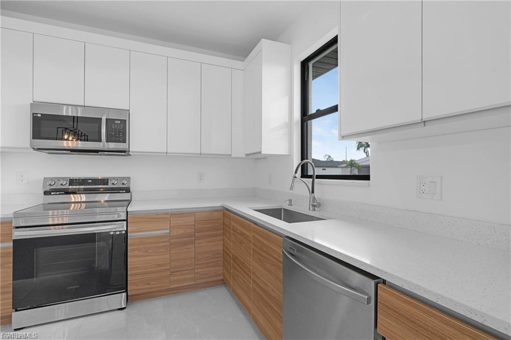 Kitchen with stainless steel appliances, modern cabinets, white cabinetry, and light stone countertops