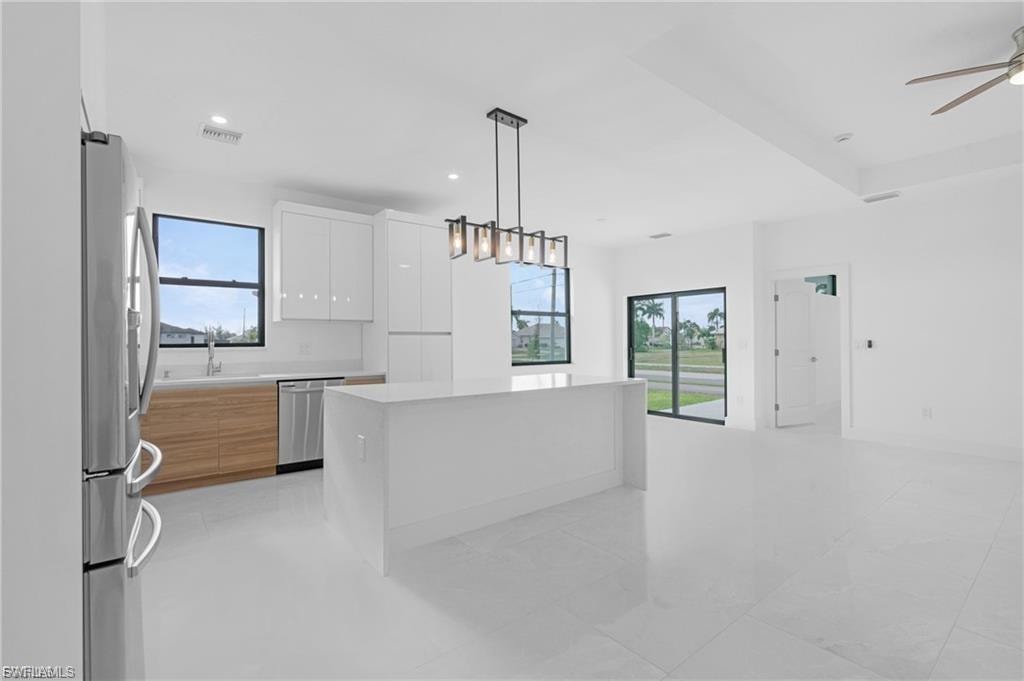 Dual tone kitchen featuring a kitchen island, stainless steel appliances, two tone cabinets, modern cabinets, and ceiling fan