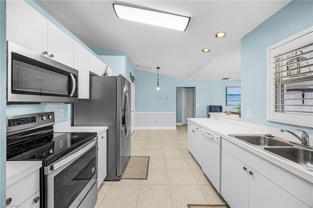 Kitchen with stainless steel appliances, light countertops, white cabinetry, decorative light fixtures, and light tile patterned flooring