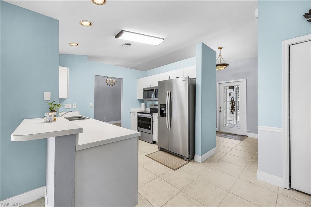 Kitchen with stainless steel appliances, light countertops, white cabinetry, a kitchen bar, and a peninsula