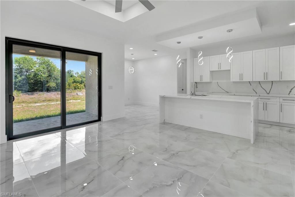 Kitchen with light stone countertops, an island with sink, white cabinetry, and light marble finish floors