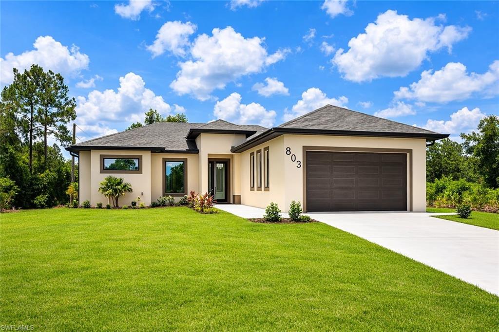 Prairie-style house with an attached garage, a front yard, stucco siding, and concrete driveway