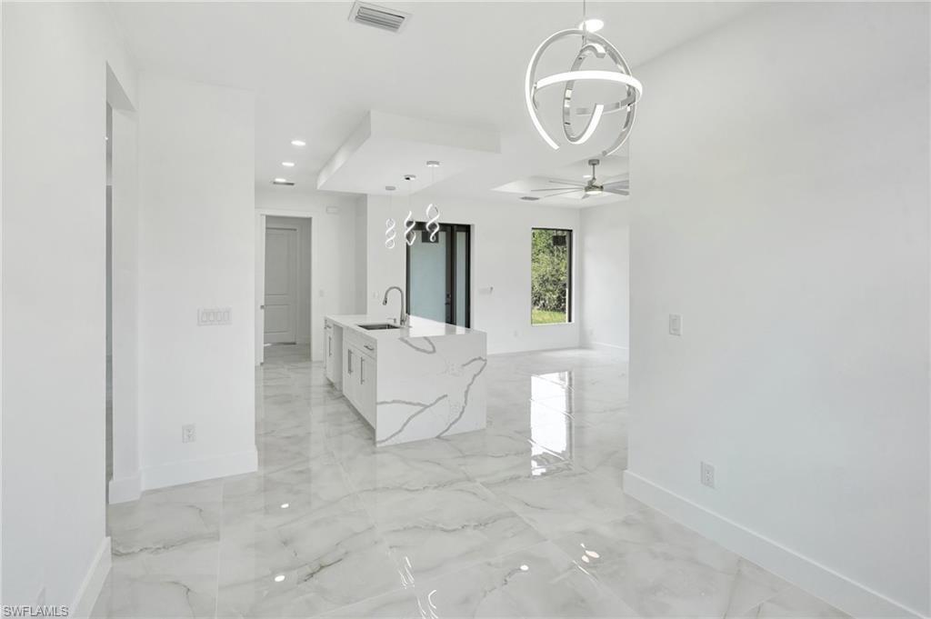 Empty room featuring a chandelier, light marble finish floors, and ceiling fan