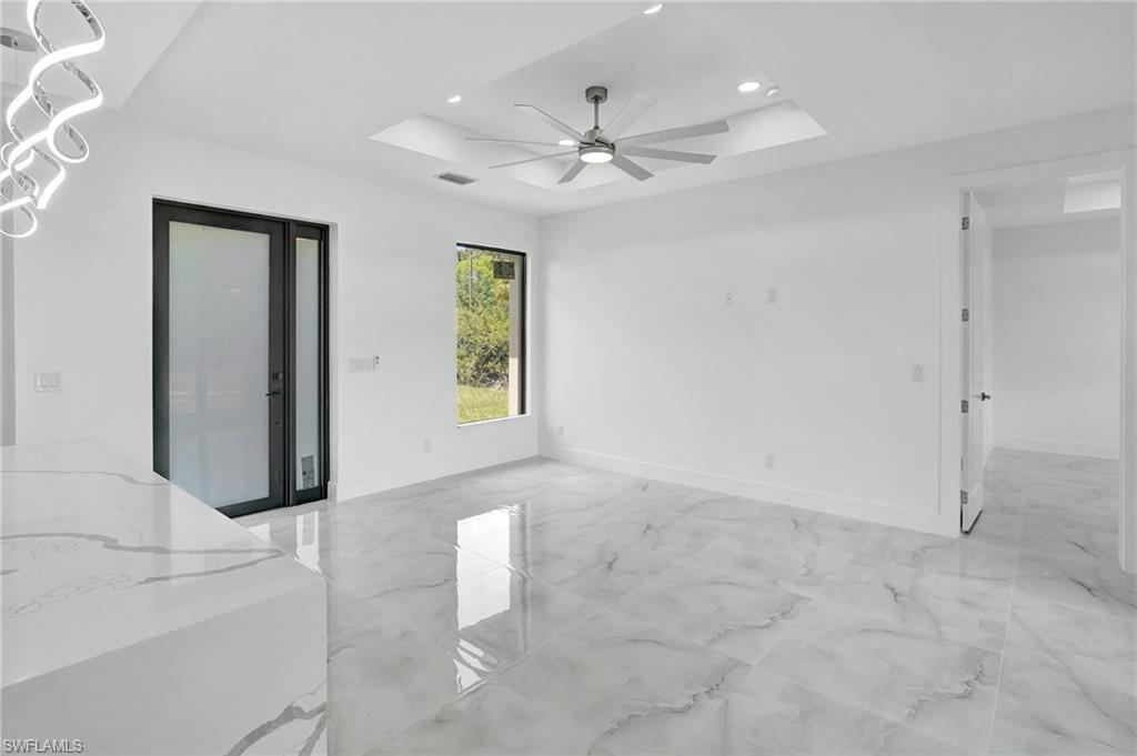 Unfurnished room with a raised ceiling, light marble finish floors, ceiling fan, and recessed lighting