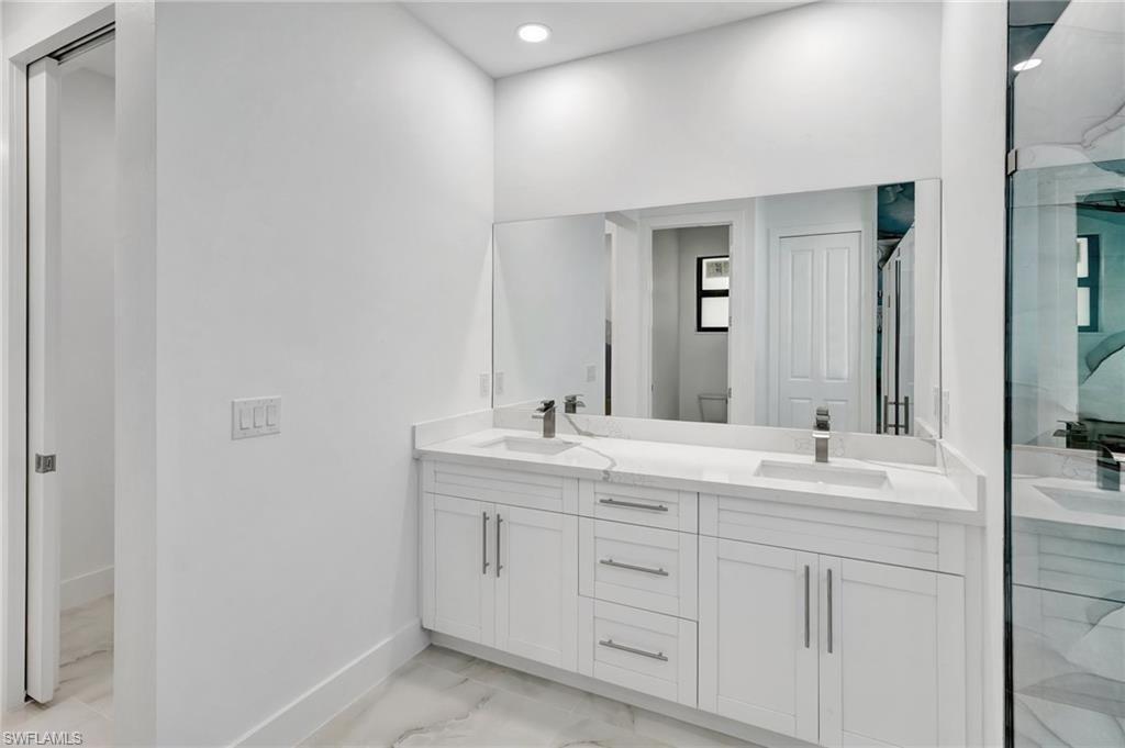 Full bath with double vanity, a marble finish shower, light marble finish flooring, and recessed lighting
