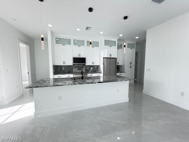 Kitchen with white cabinets, glass fronted cabinets, a large island with sink, and stainless steel appliances