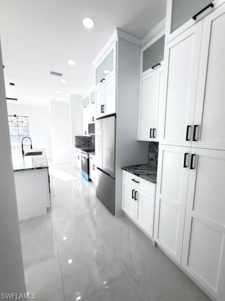 Kitchen featuring glass fronted cabinets, white cabinets, stainless steel appliances, dark stone counters, and pendant lighting
