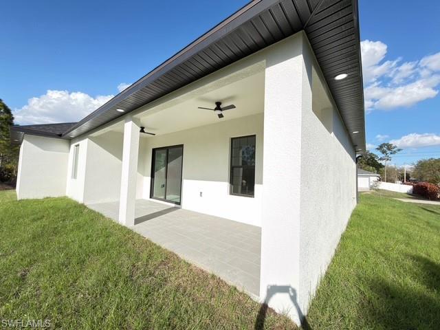 Rear view of house featuring a yard, a ceiling fan, stucco siding, and a patio area