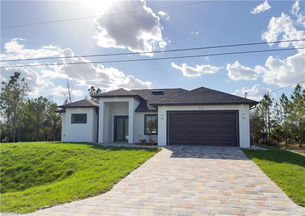 Prairie-style home featuring a front yard, stucco siding, a garage, decorative driveway, and roof with shingles