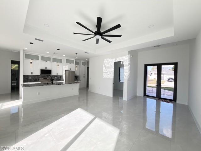 Unfurnished living room featuring plenty of natural light, ceiling fan, french doors, light marble finish flooring, and a raised ceiling