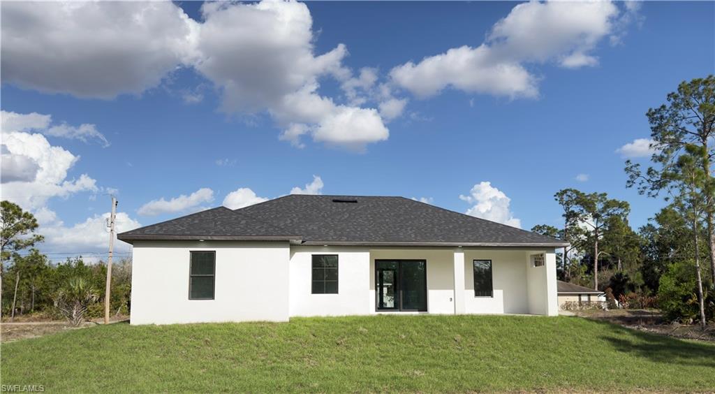 Back of property featuring stucco siding, a patio, a lawn, and roof with shingles