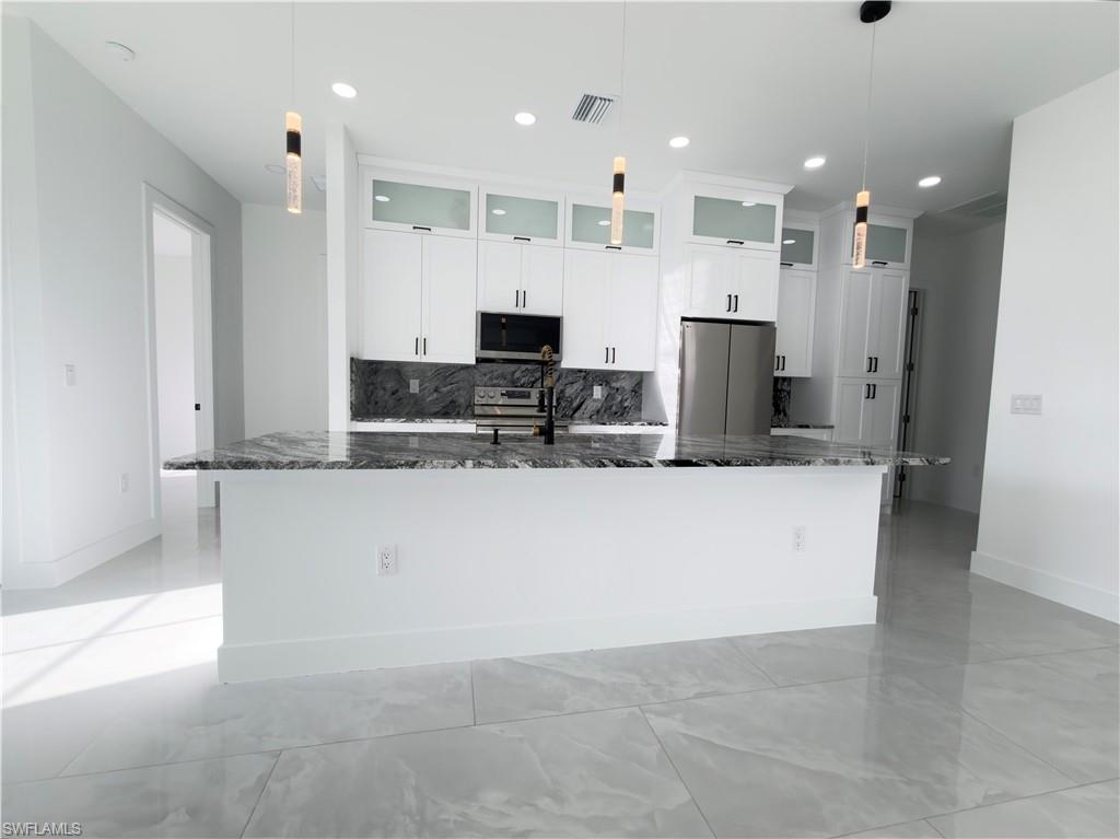 Kitchen featuring white cabinetry, decorative backsplash, stainless steel appliances, and glass fronted cabinets