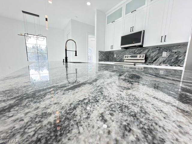 Kitchen featuring glass fronted cabinets, white cabinetry, light stone countertops, stainless steel electric stove, and decorative light fixtures