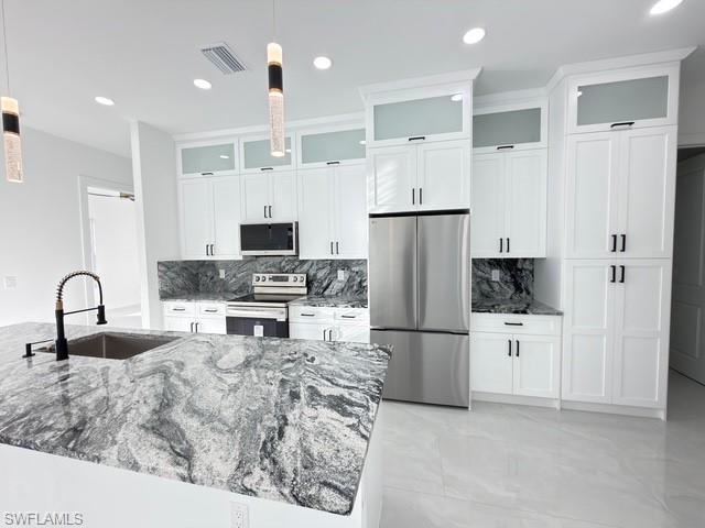 Kitchen with glass fronted cabinets, stainless steel appliances, decorative backsplash, and pendant lighting