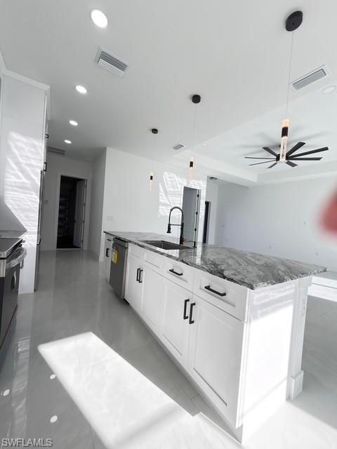 Kitchen featuring decorative light fixtures, white cabinetry, dark stone counters, stainless steel appliances, and an island with sink