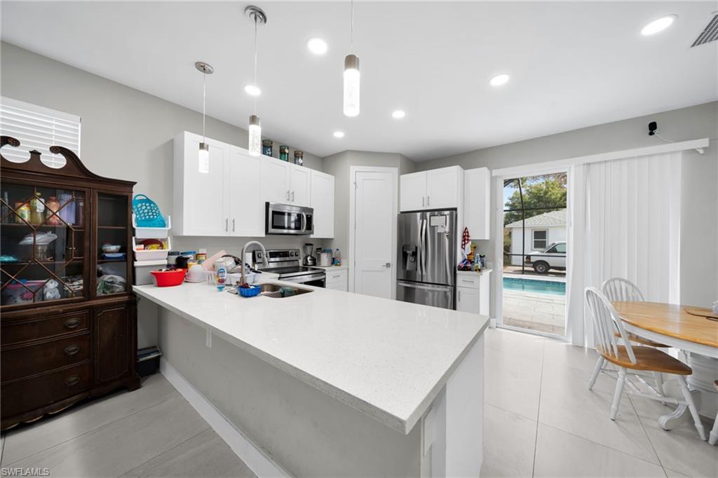 Kitchen featuring stainless steel appliances, a peninsula, white cabinets, hanging light fixtures, and light stone countertops