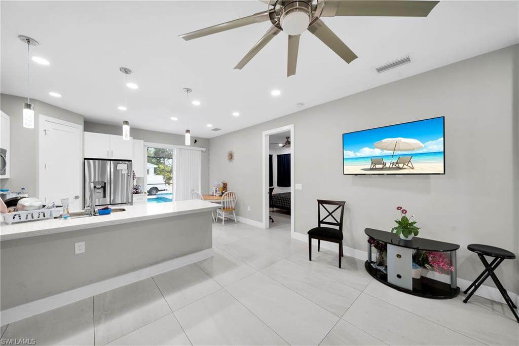 Kitchen with stainless steel fridge with ice dispenser, white cabinets, pendant lighting, ceiling fan, and light stone counters