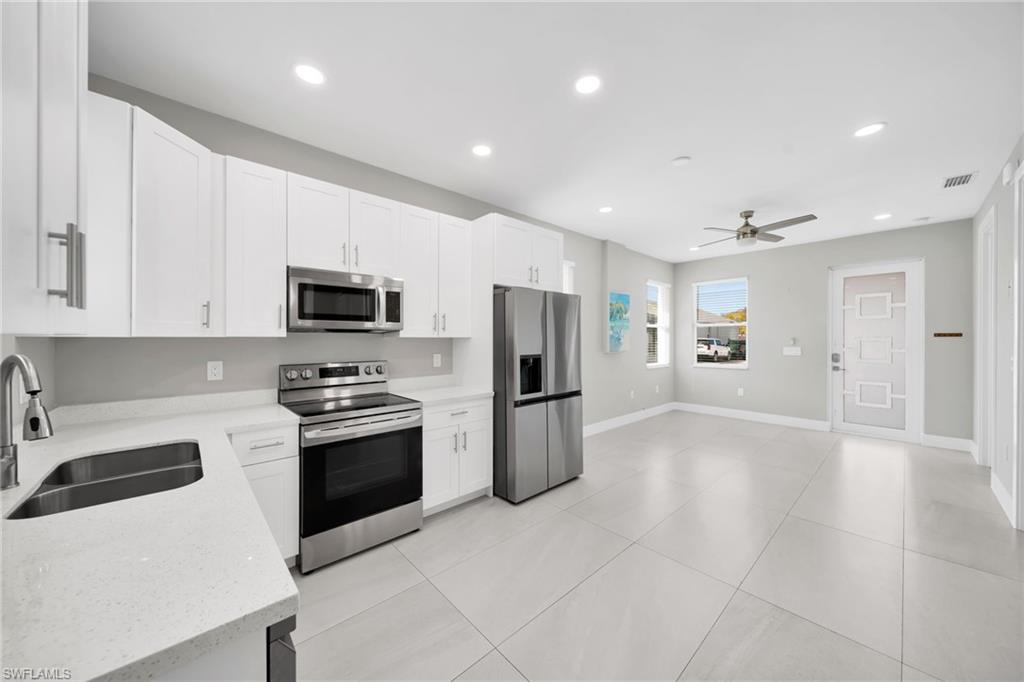Kitchen featuring stainless steel appliances, recessed lighting, white cabinetry, light stone countertops, and ceiling fan