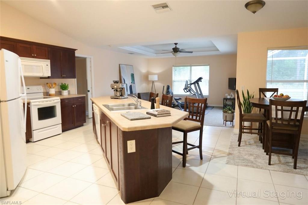 Kitchen with light countertops, white appliances, a breakfast bar area, dark wood finish cabinets, and an island with sink