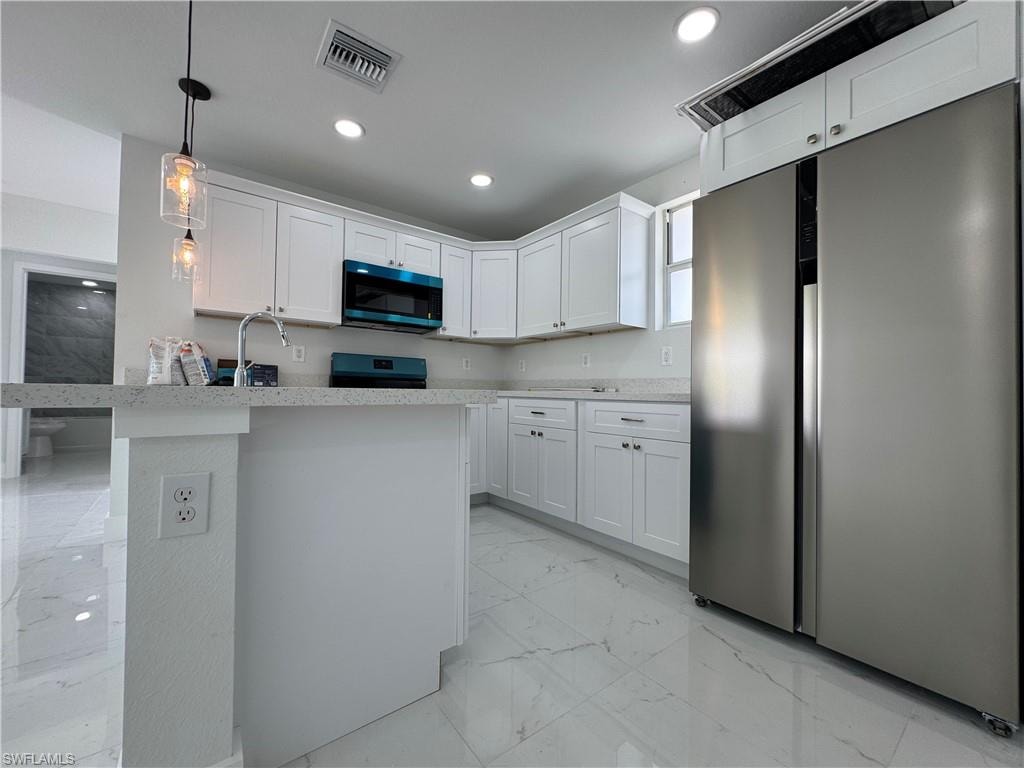 Kitchen with stainless steel fridge, light marble finish flooring, white cabinetry, decorative light fixtures, and range