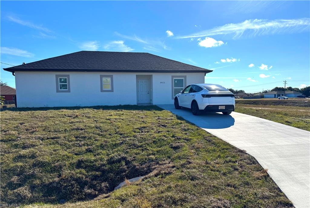 Ranch-style home with stucco siding, a front yard, roof with shingles, and driveway