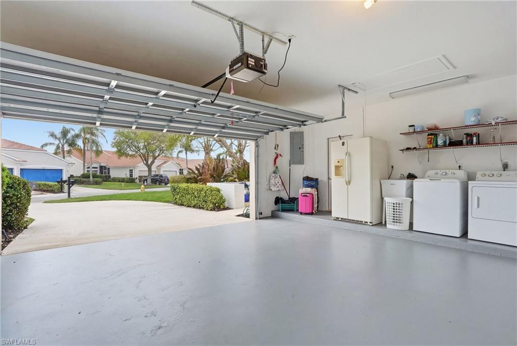Garage featuring white refrigerator with ice dispenser, washer and dryer, electric panel, a residential view, and a garage door opener