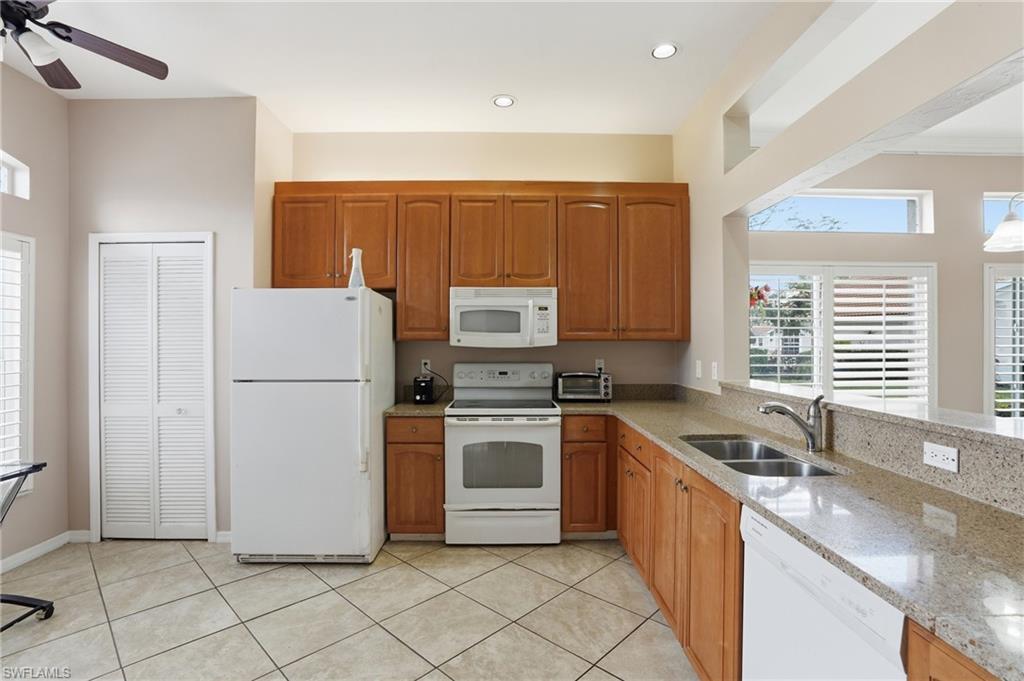 Kitchen with light stone counters, white appliances, wood finish cabinets, a ceiling fan, and light tile patterned flooring