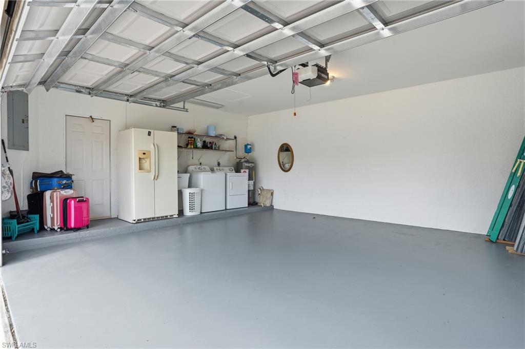 Garage with white refrigerator with ice dispenser, washing machine and dryer, electric water heater, electric panel, and a garage door opener