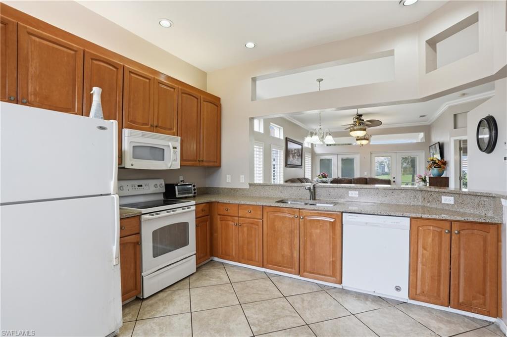 Kitchen featuring white appliances, wood finish cabinets, suspended lighting, light stone countertops, and ornamental molding