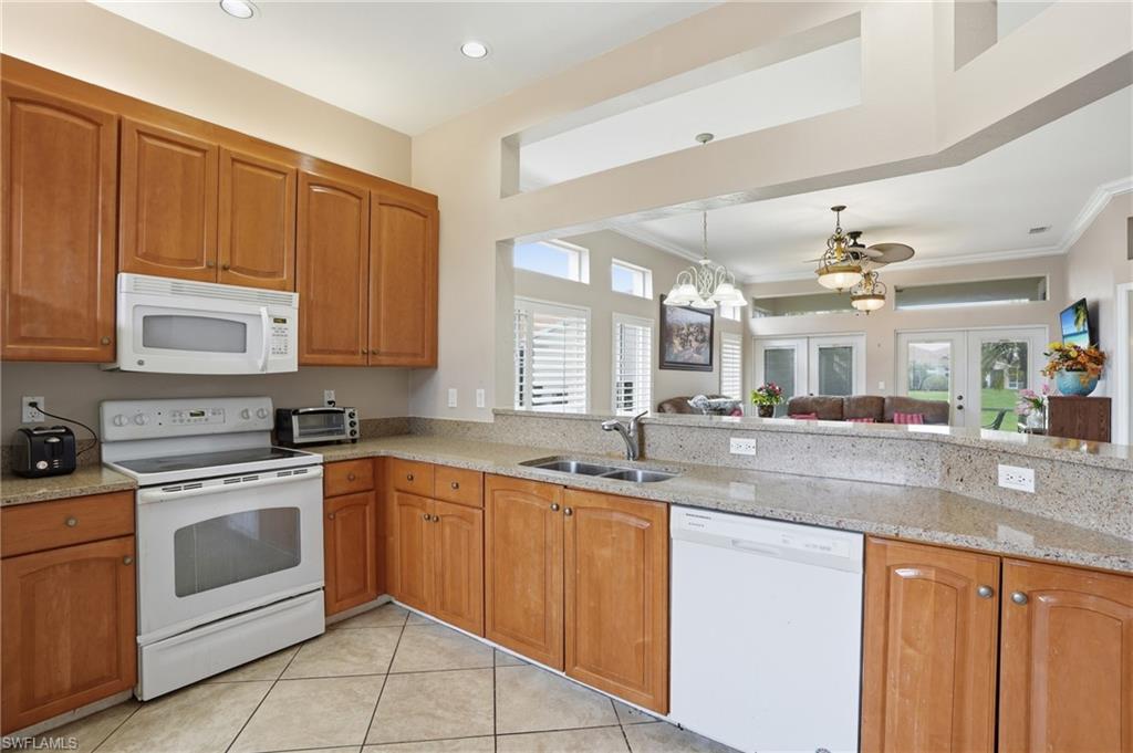 Kitchen featuring white appliances, light stone counters, wood finish cabinets, open floor plan, and a ceiling fan