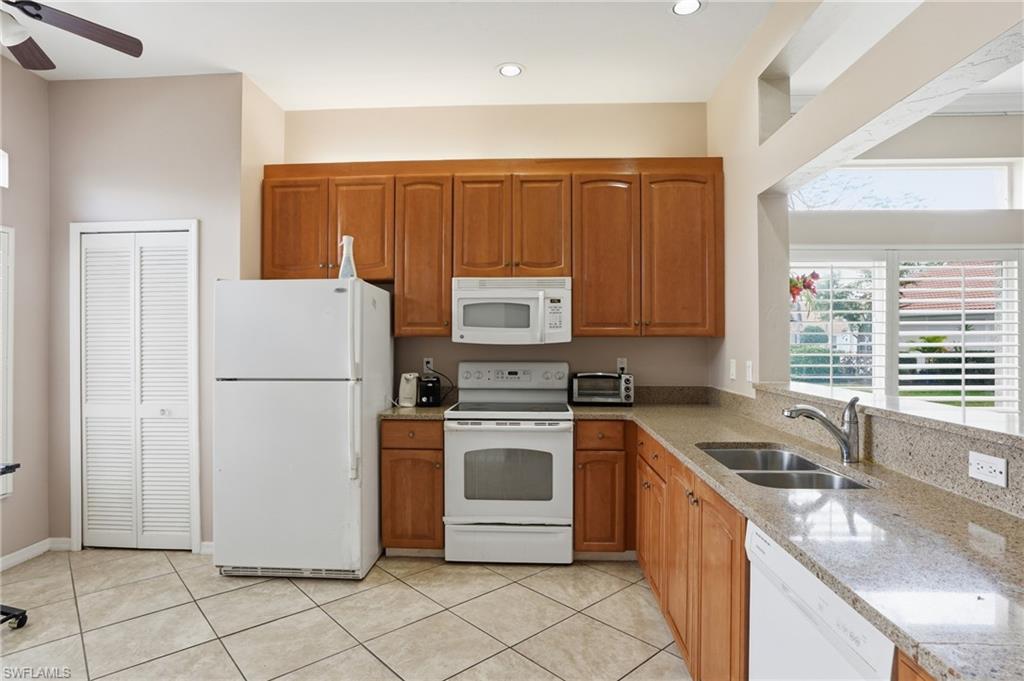 Kitchen with light stone counters, white appliances, wood finish cabinetry, and a ceiling fan