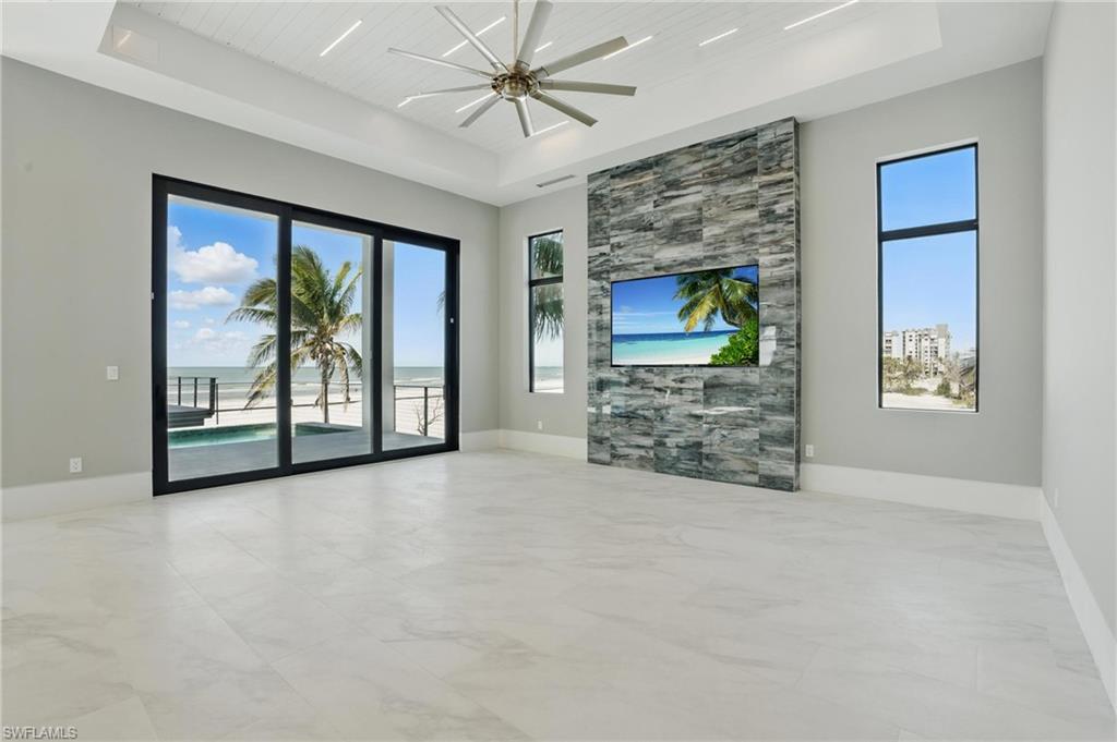 Unfurnished living room featuring a wooden tray ceiling, plenty of natural light, ceiling fan, and light marble finish flooring Virtually Enhanced