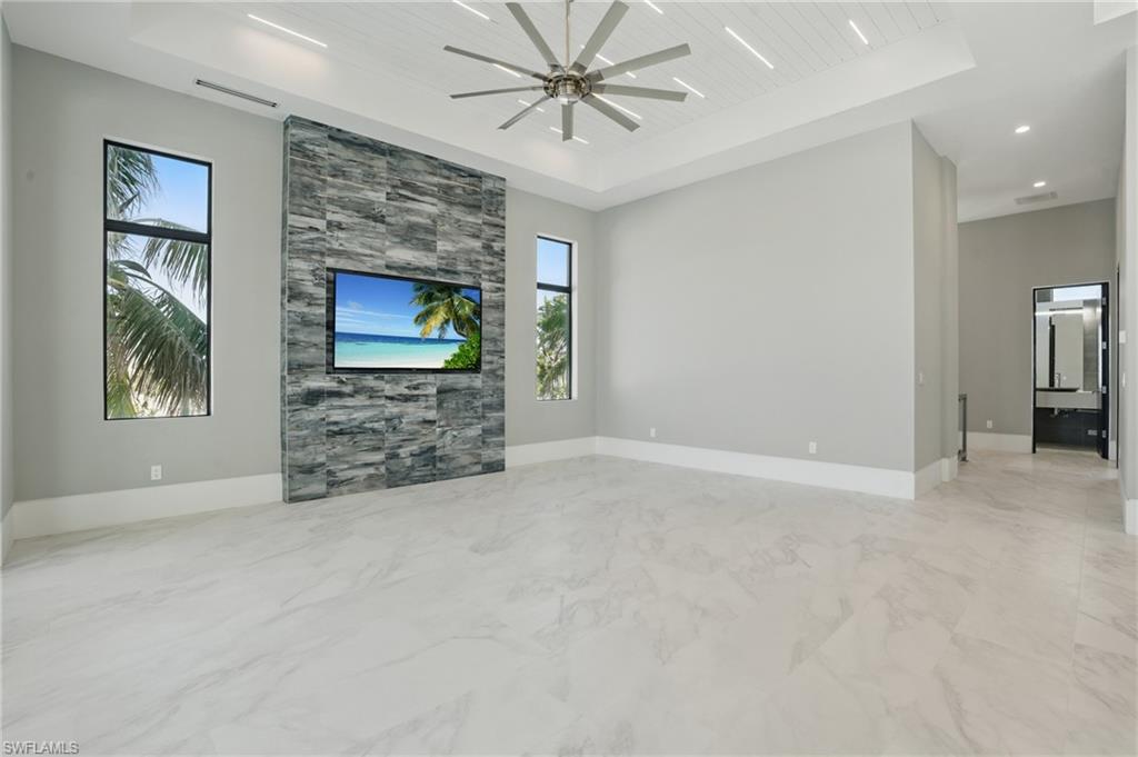 Unfurnished living room with a wooden tray ceiling, a ceiling fan, and light marble finish floorsVirtually Enhanced