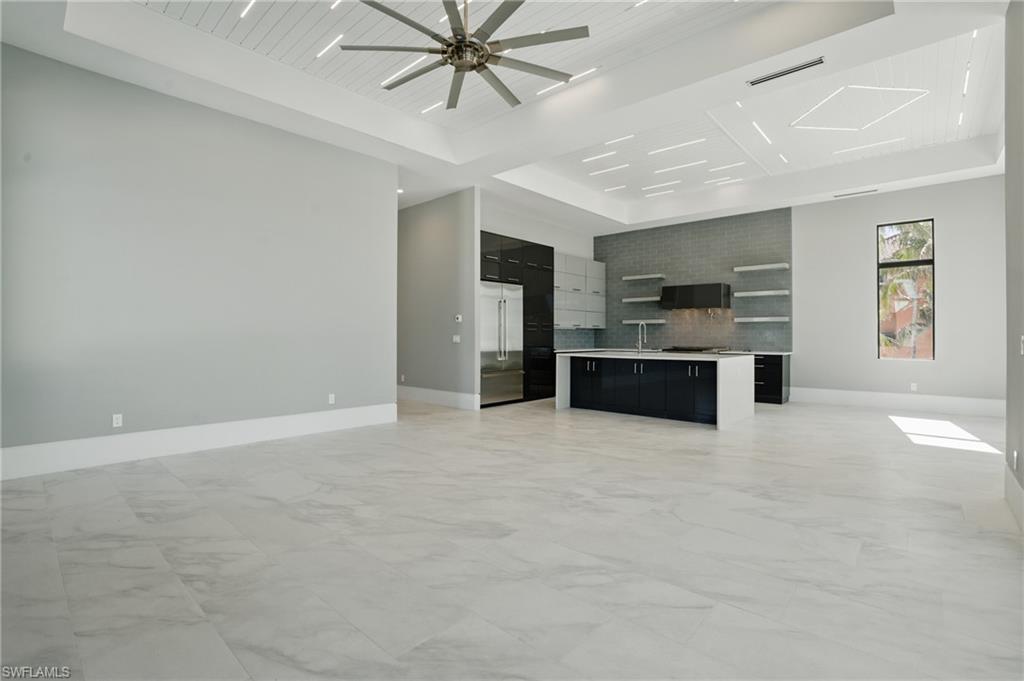 Unfurnished living room featuring light marble finish floors, a wooden tray ceiling, and ceiling fanVirtually Enhanced