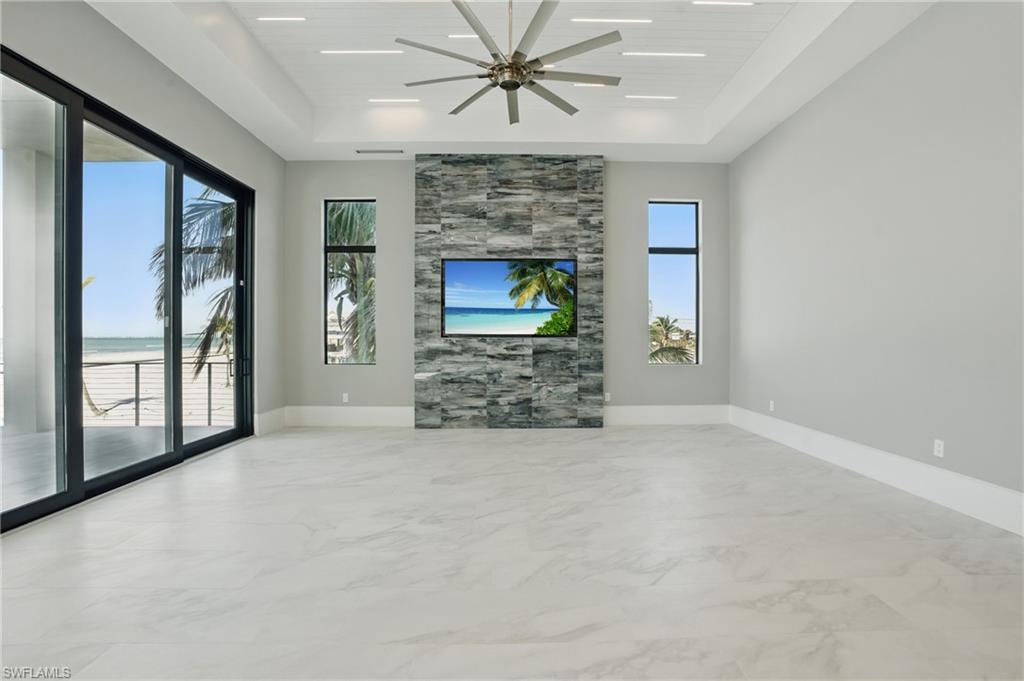 Unfurnished living room featuring a tray ceiling, light marble finish flooring, and a ceiling fan Virtually Enhanced