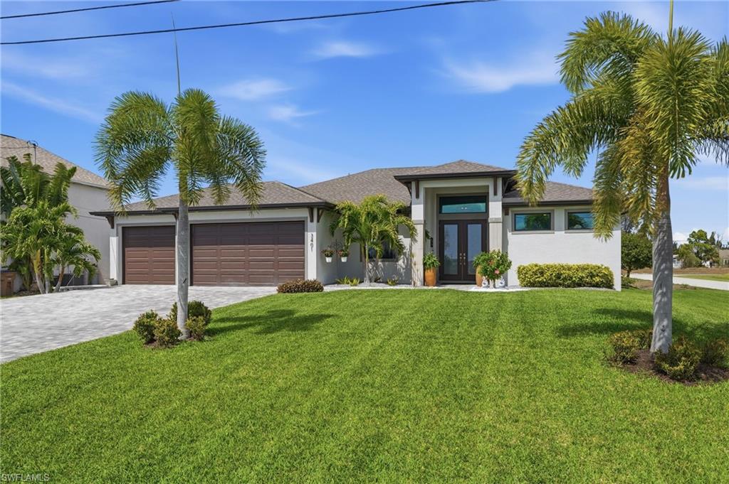 View of front facade with double glass doors, decorative driveway, a garage, a front lawn, and stucco siding