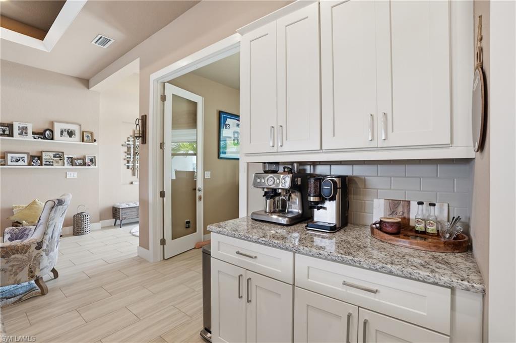 Kitchen with light stone counters, white cabinetry, decorative backsplash, and wood ceramic tiled floors