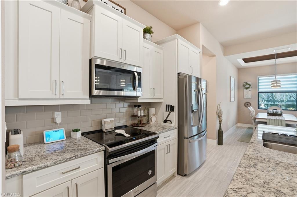 Kitchen with stainless steel appliances, white cabinets, light stone countertops, and decorative backsplash