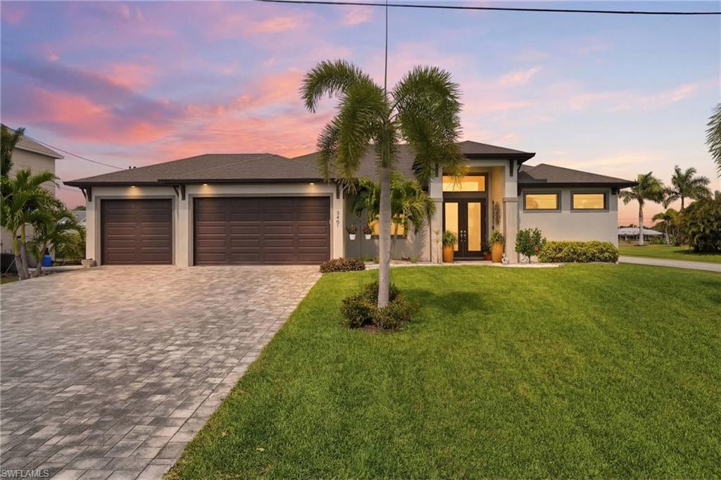 Prairie-style home featuring decorative driveway, a garage, soffit lighting, stucco siding, glass doors, and a front lawn
