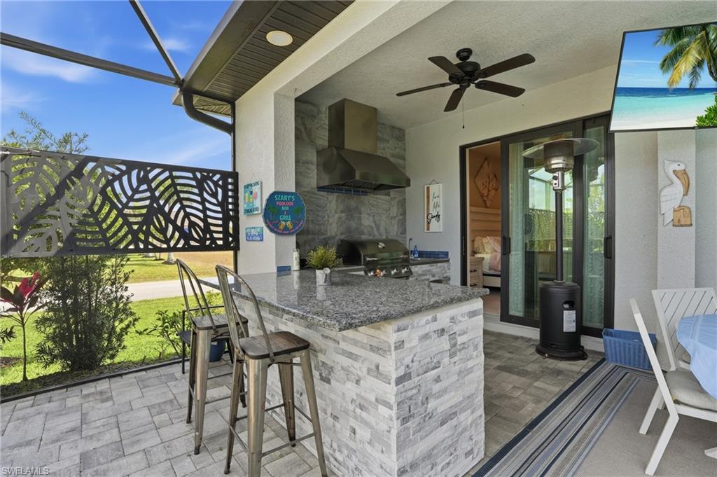 View of outdoor kitchen with ceiling fan, area for grilling, and a lanai