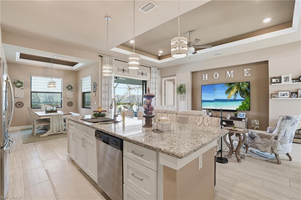 Kitchen featuring a tray ceiling, stainless steel appliances, light stone counters, a kitchen island with sink, and white cabinets