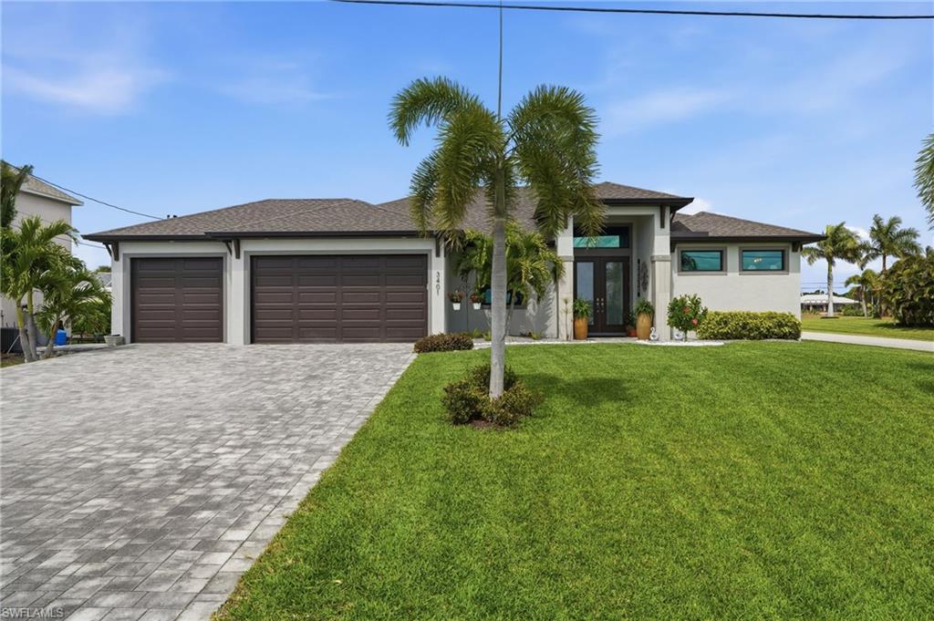 Prairie-style home with decorative driveway, an attached garage, double glass doors, a front yard, and stucco siding