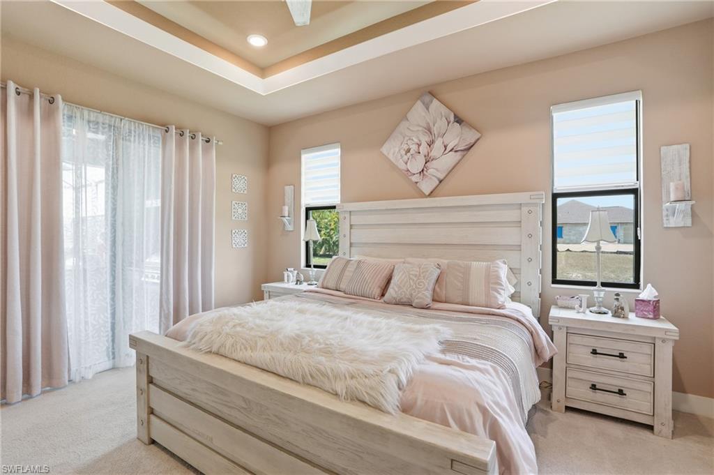 Bedroom with light colored carpet, a raised ceiling, and ceiling fan