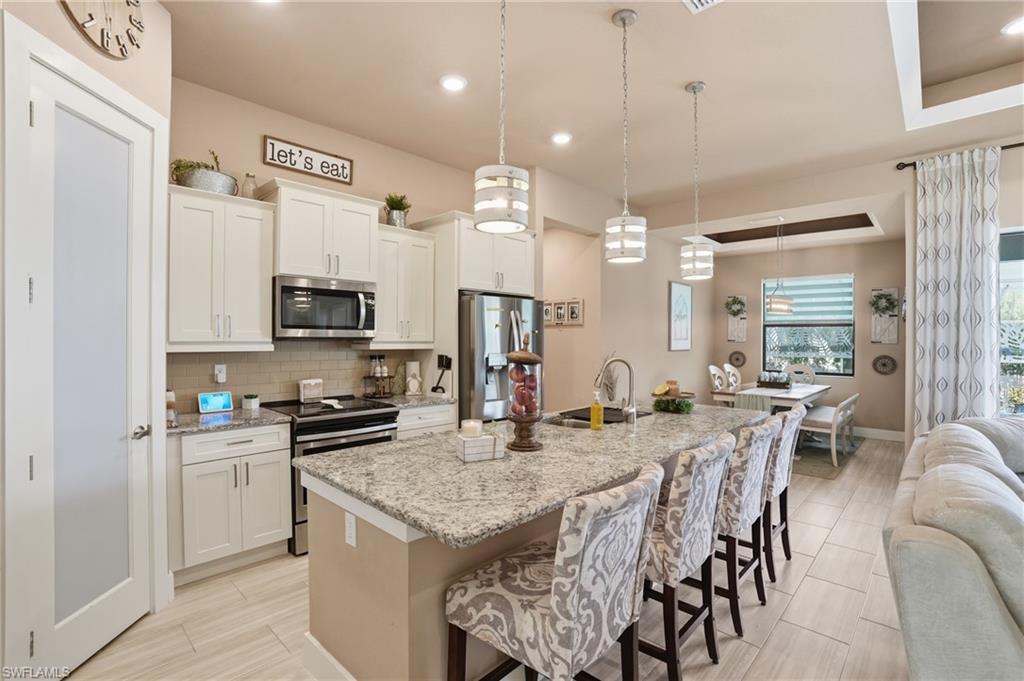Kitchen with stainless steel appliances, open floor plan, a kitchen breakfast bar, light stone countertops, and an island with sink