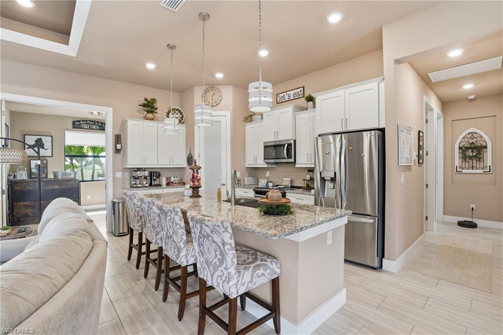 Kitchen with a kitchen breakfast bar, open floor plan, stainless steel appliances, light stone countertops, and a kitchen island with sink, flex room/den off the main living area