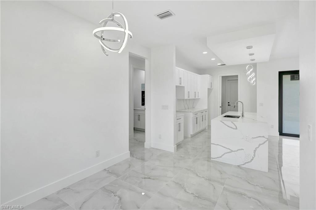 Kitchen featuring white cabinets, hanging light fixtures, light stone countertops, light marble finish floors, and a kitchen island with sink