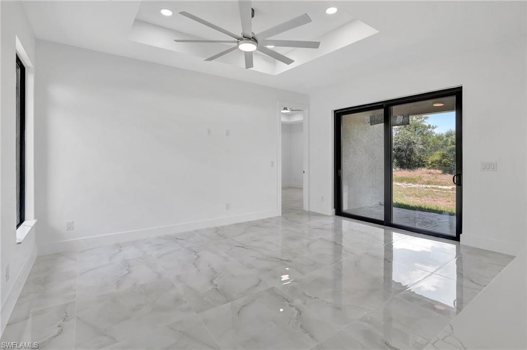 Spare room featuring a tray ceiling, a ceiling fan, light marble finish flooring, and recessed lighting