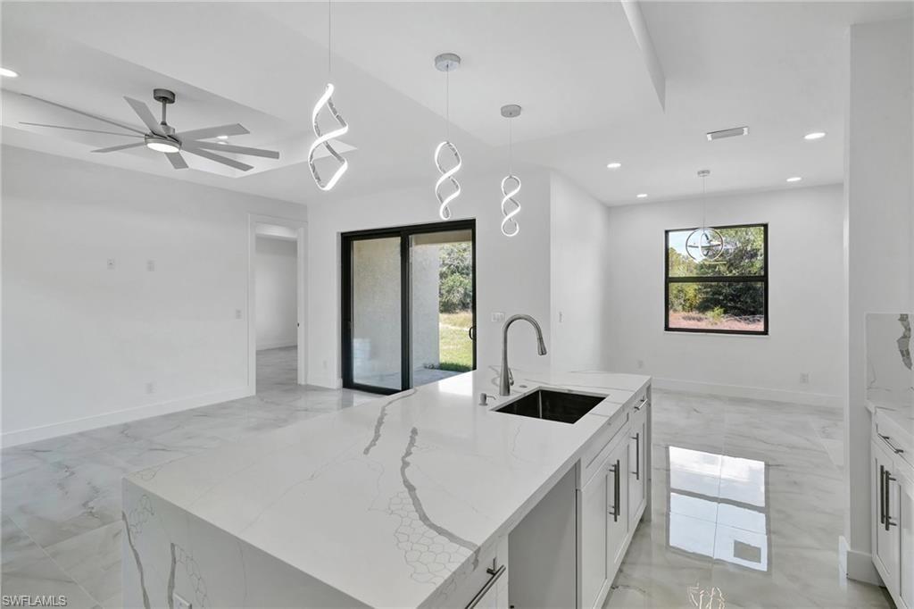 Kitchen with light stone countertops, a kitchen island with sink, and hanging light fixtures