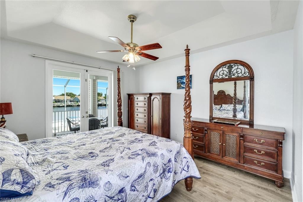Bedroom featuring ceiling fan, a water view, light wood-style flooring, a tray ceiling, and access to outside