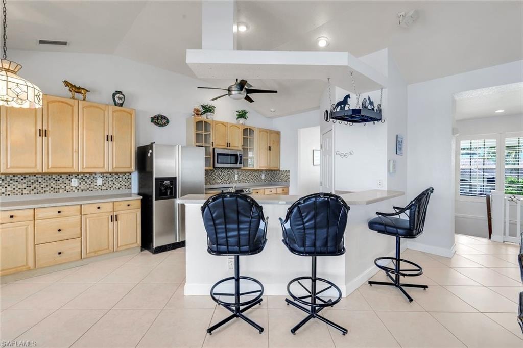 Kitchen featuring glass fronted cabinets, light wood finish cabinets, a kitchen bar, light countertops, and stainless steel appliances
